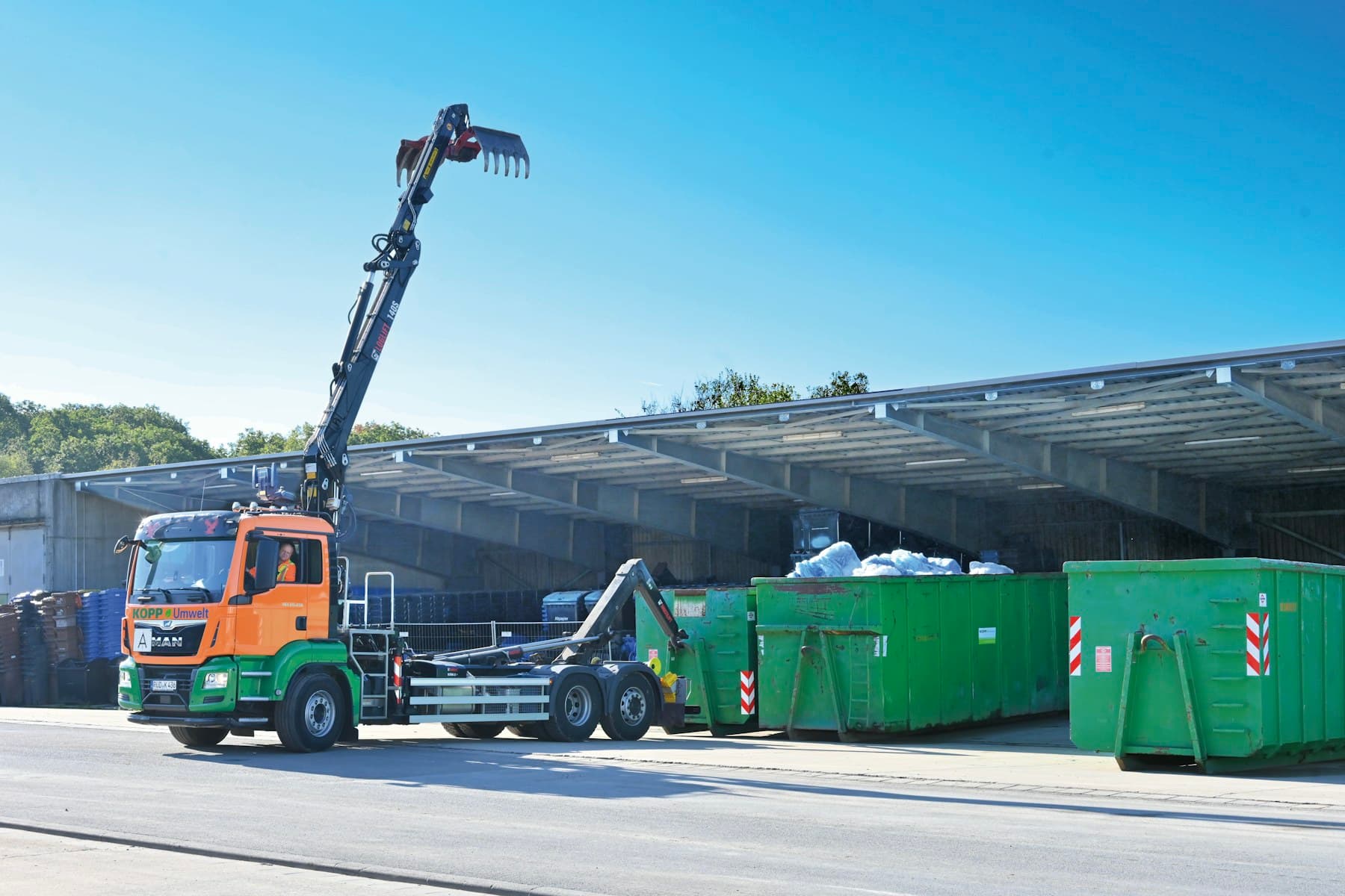 Truck-mounted crane vehicle operating beside industrial containers